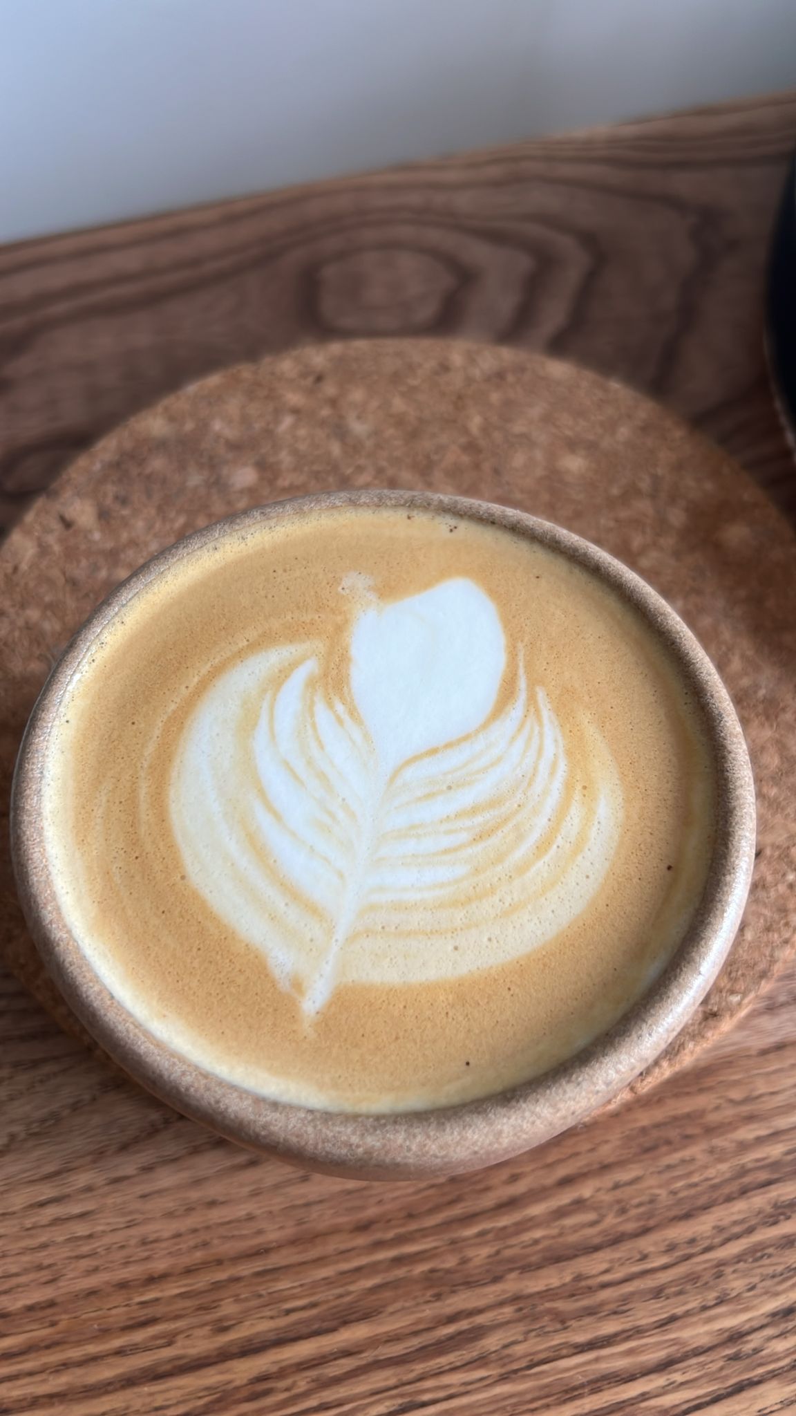 Latte art feather pour in a rustic ceramic cup on a wooden tray